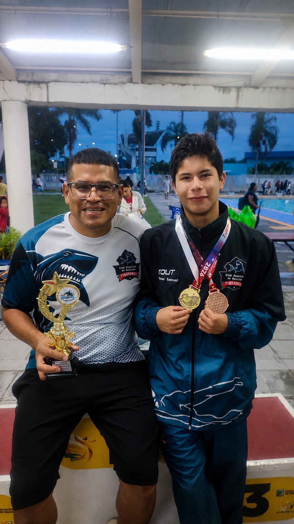 Entrenador del club junto a un nadador con su trofeo y medallas