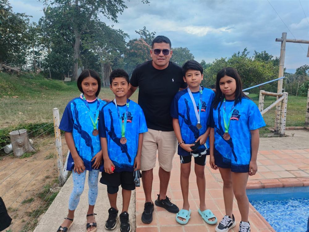 Entrenador junto a cuatro nadadores del club con medalla de bronce