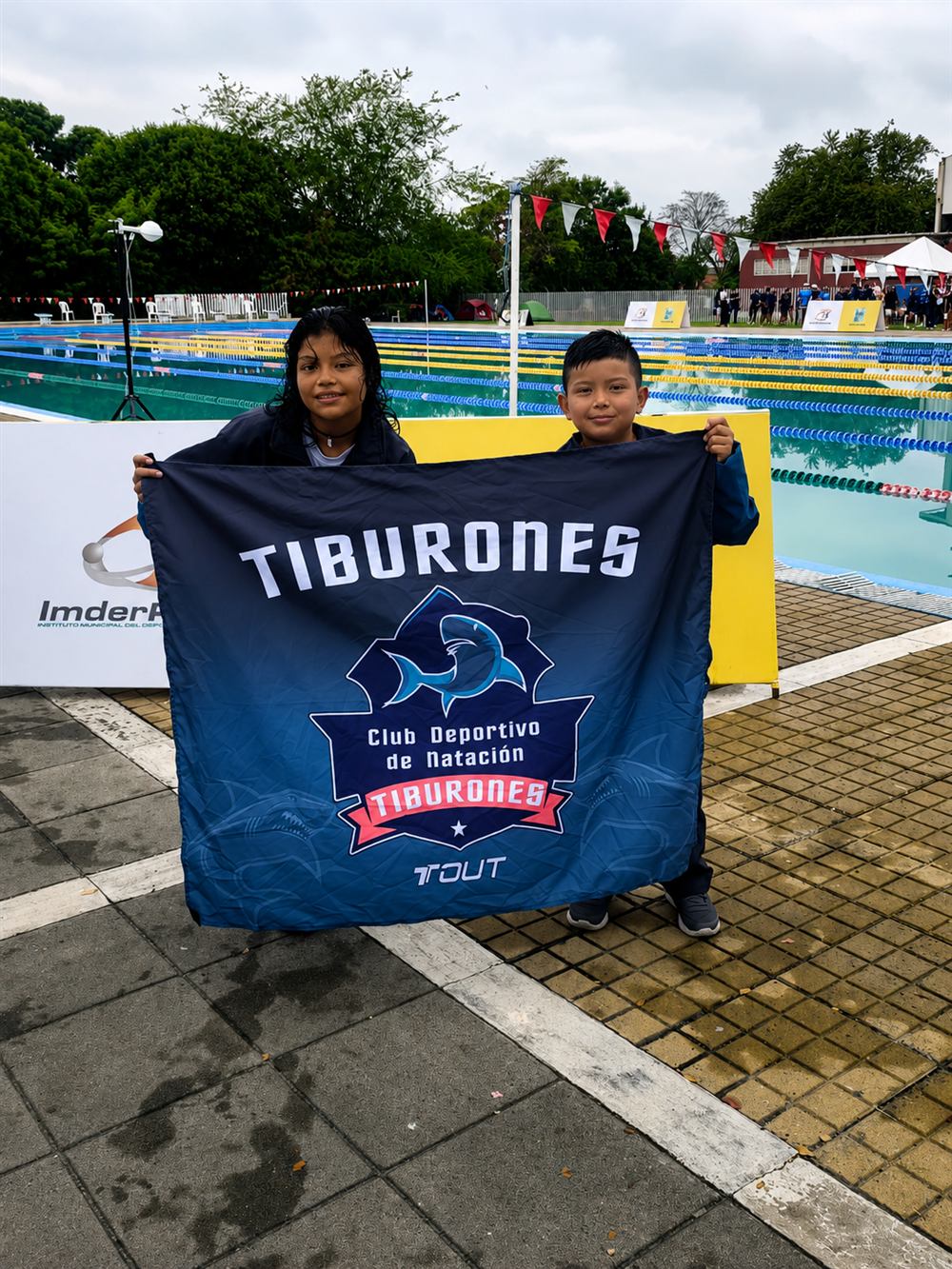 Dos nadadores del club sosteniendo la bandera de Tiburones en un evento