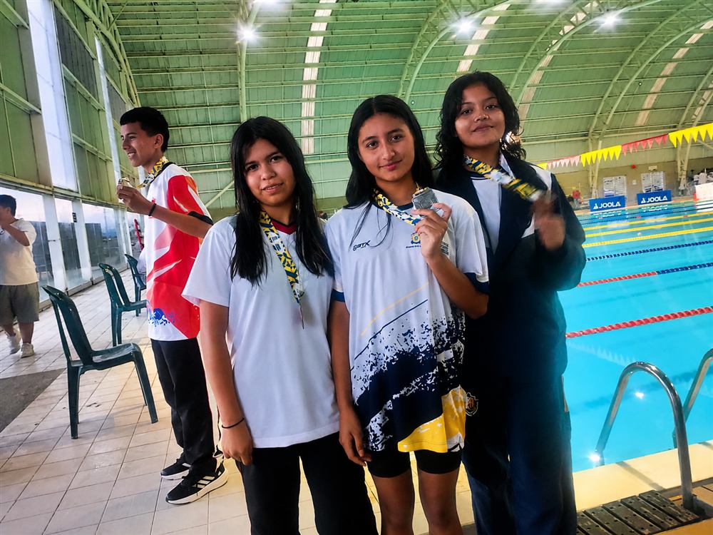 Cuatro nadadores del club con sus medallas en una piscina cubierta