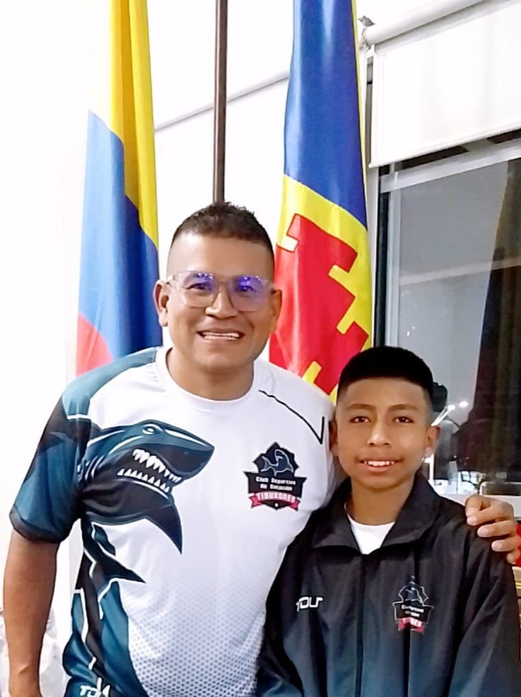 Entrenador del club junto a un nadador, con banderas de fondo